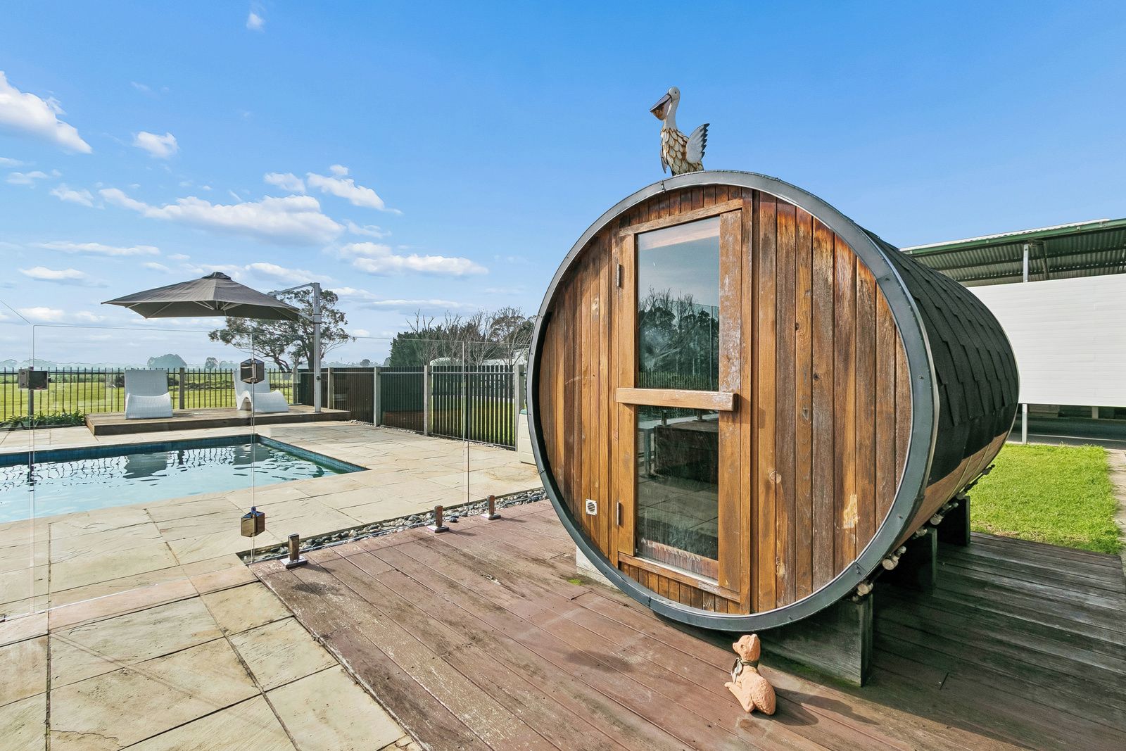 A wooden barrel-shaped structure with a glass door, a pool, and a fenced outdoor area.
