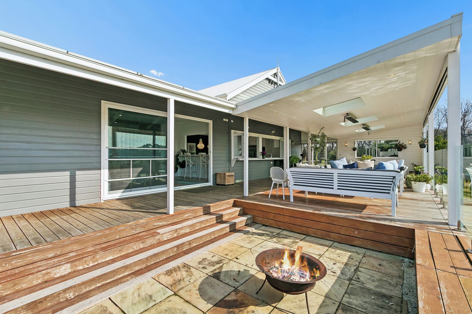 A modern outdoor deck with a fire pit, a covered seating area, and a glass door leading to a patio.