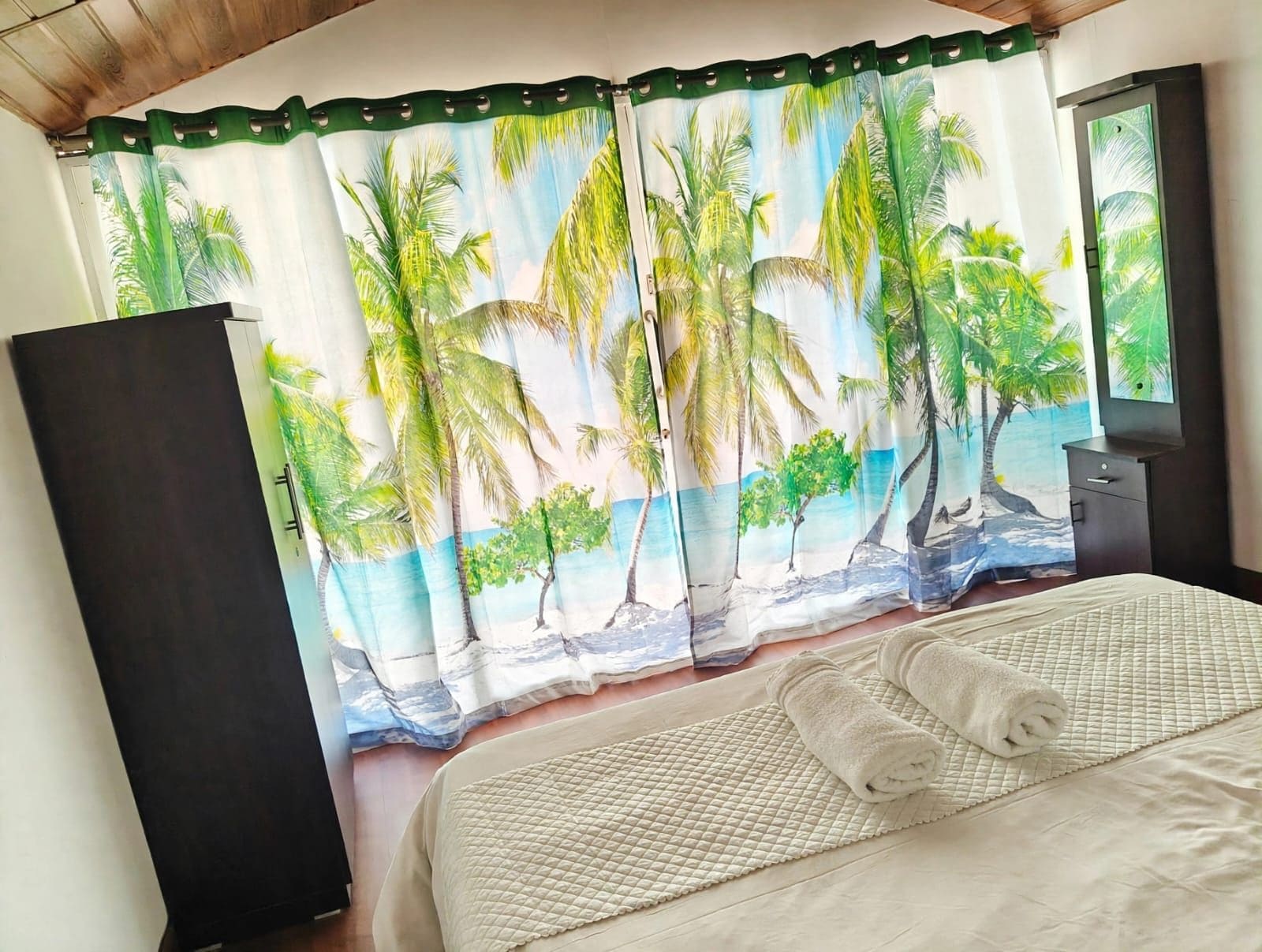 Un dormitorio con cama, mesita de noche, cómoda y ventana con vistas a palmeras.