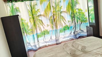 A bedroom with a bed, a nightstand, a dresser, and a window with a view of palm trees.