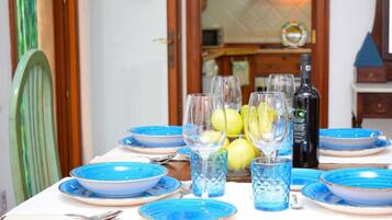 A dining table set with blue plates and glasses, a bottle of wine, and a bowl of lemons.