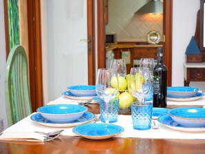 A dining table set with blue plates and glasses, a bottle of wine, and a bowl of lemons. - Holiday Home in Muro With Swimming Pool (Muro)