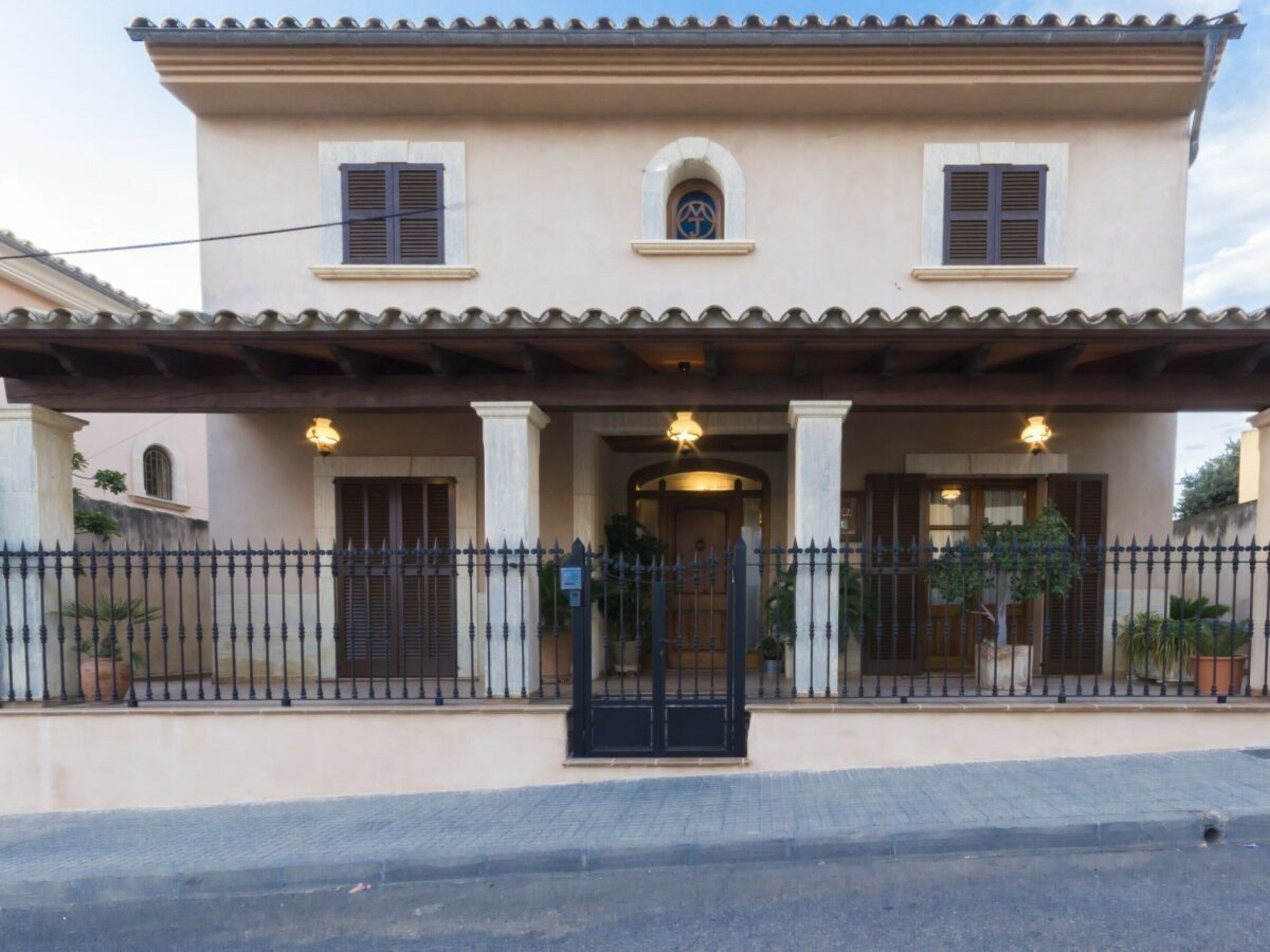 A two-story building with a tiled roof, a central entrance with a black gate, and a small arched window above the door.
