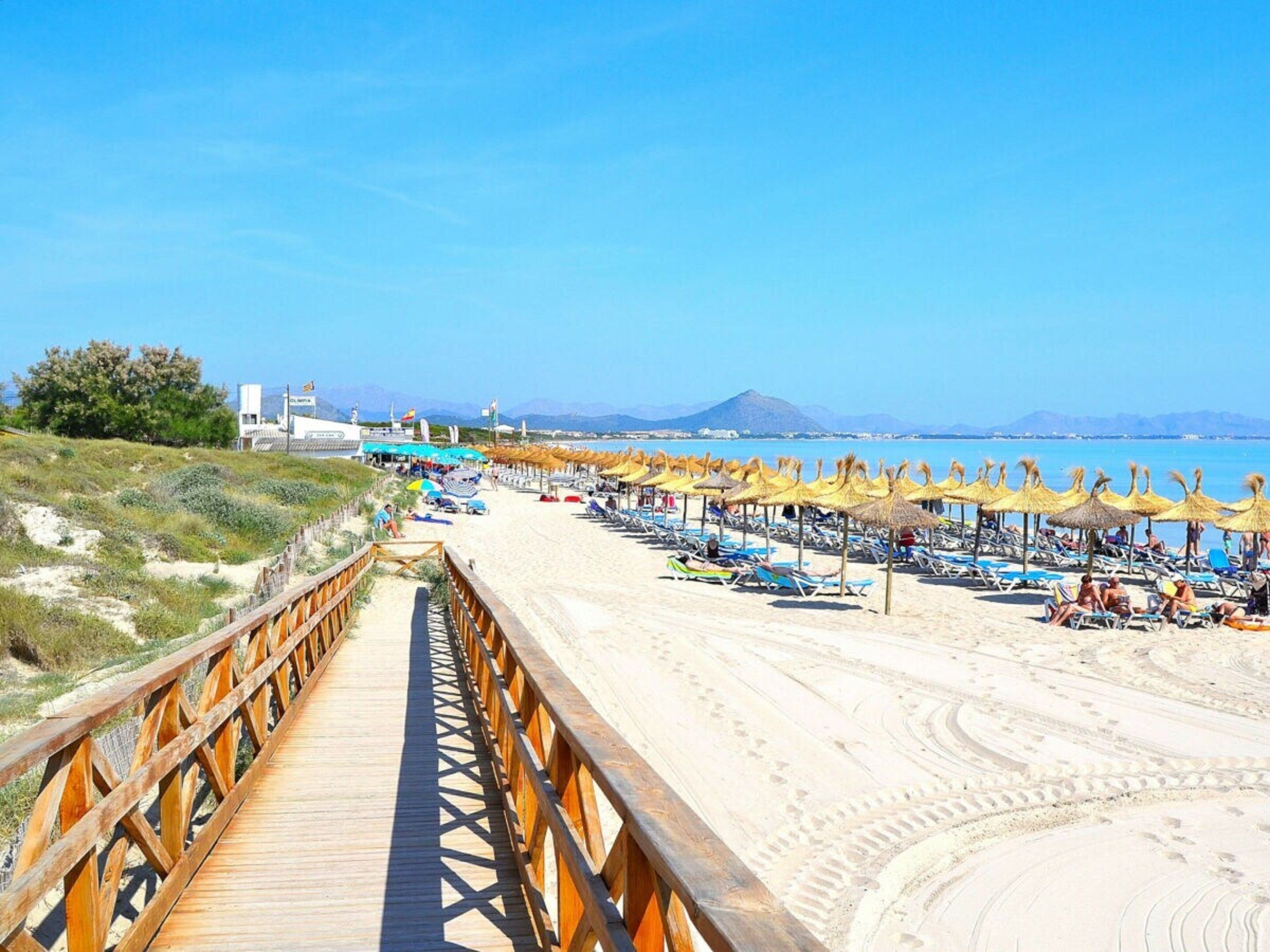 A beach with a wooden boardwalk leading to beach umbrellas and lounge chairs.