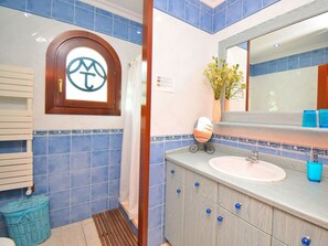 A bathroom with blue tiles, a wooden vanity, a sink, a mirror, and a window with a logo. - Holiday Home in Muro With Swimming Pool (Muro)