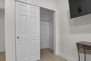 A room with a white door, a closet with hanging space, and a small table with a metal chair. - Cozy 3BR Detroit Home | Sleeps 8 | Self Check-in (Detroit)