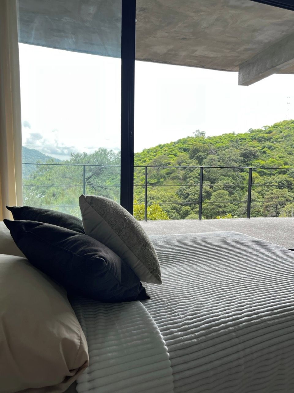 A bed with pillows and a view of a green landscape through a balcony railing.