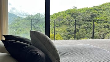 A bed with pillows and a view of a green landscape through a balcony railing.