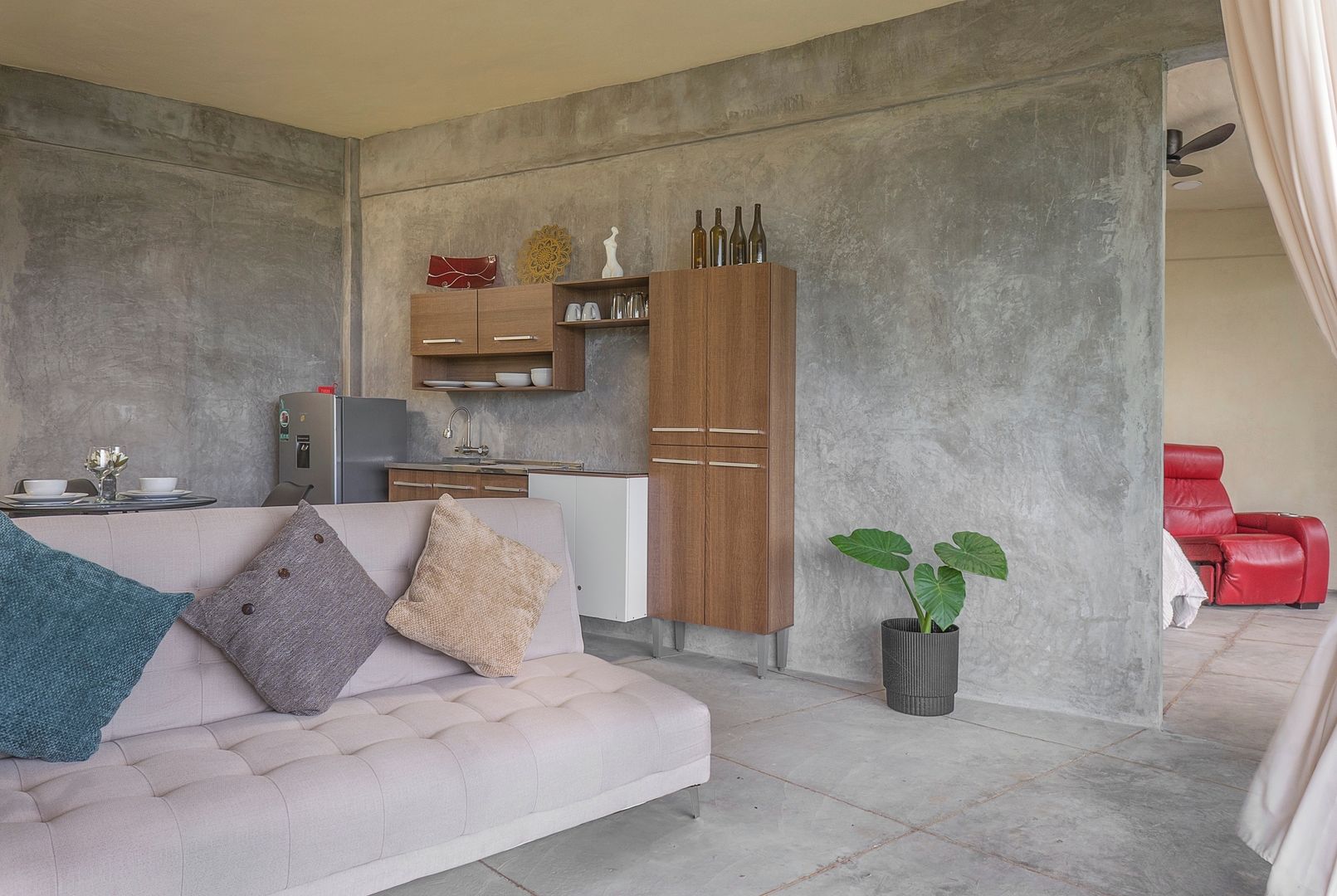 A modern living space with a sofa, a dining table, a kitchen area, and a red chair.