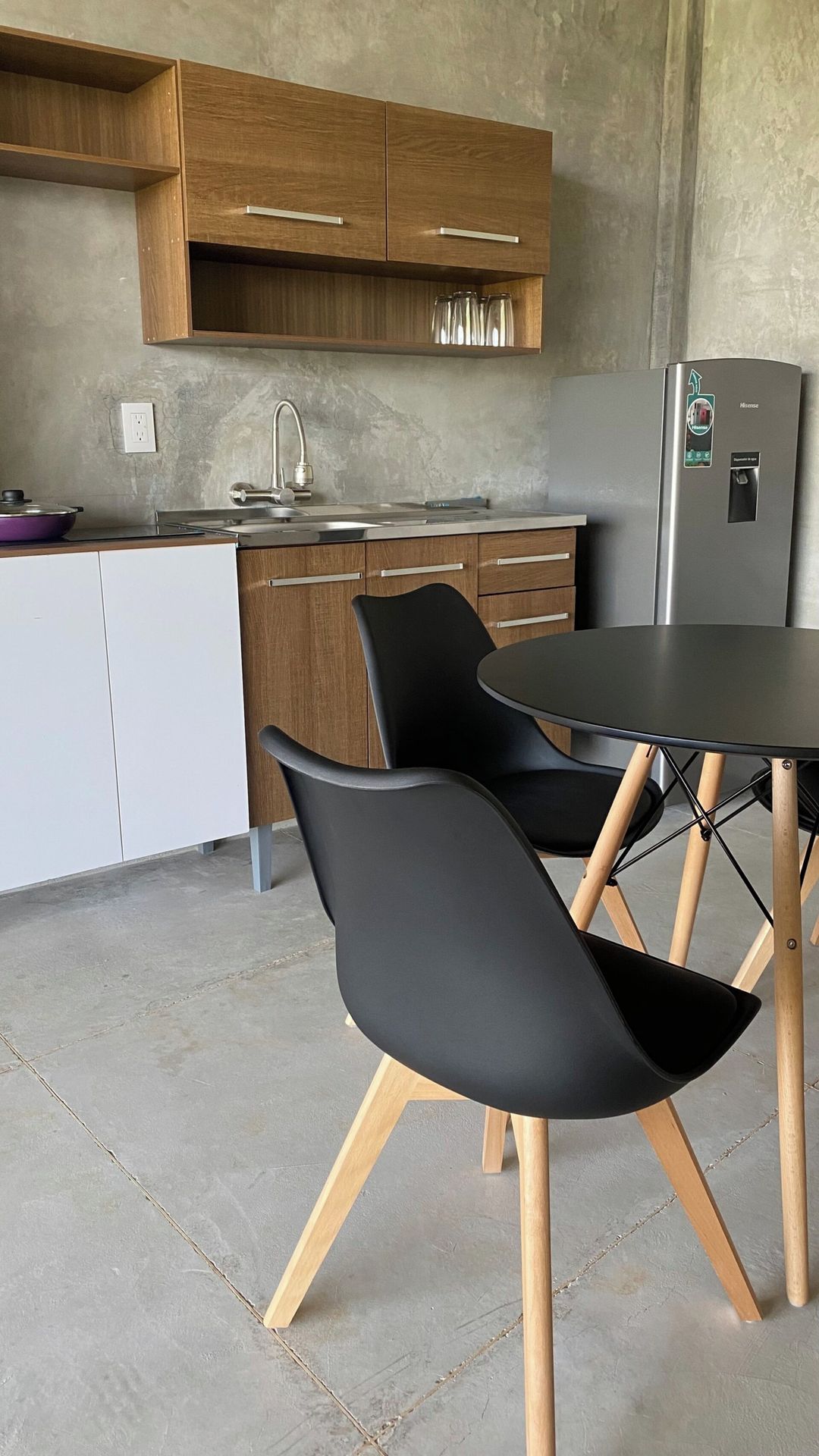 Una cocina moderna con armarios de madera, un refrigerador de acero inoxidable, un lavamanos y un comedor con una mesa redonda y dos sillas.