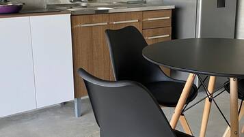 Una cocina moderna con armarios de madera, un refrigerador de acero inoxidable, un lavamanos y un comedor con una mesa redonda y dos sillas.