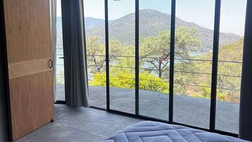 Un dormitorio con una cama grande, un armario de madera y vistas a un paisaje montañoso a través de ventanales de techo a piso.
