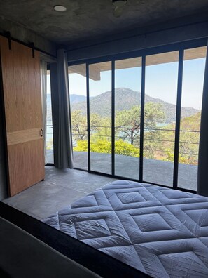 Un dormitorio con una cama grande, un armario de madera y vistas a un paisaje montañoso a través de ventanales de techo a piso.