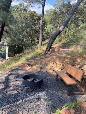 A fire pit with logs, surrounded by gravel, next to a wooden bench and a stone wall. - Modern Loft - Spectacular Mountain and Lake Views (Valle de Bravo)