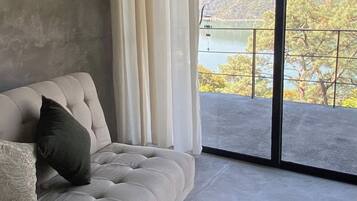 Ein Zimmer mit einer Couch, Blick auf einen See und eine Berglandschaft.
