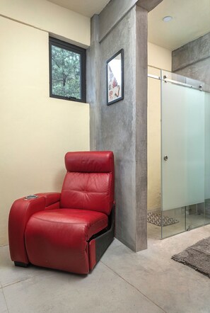Ein roter Massagesessel in einem Raum mit einer Betonsäule, einer Glastür und einem gerahmten Bild an der Wand.