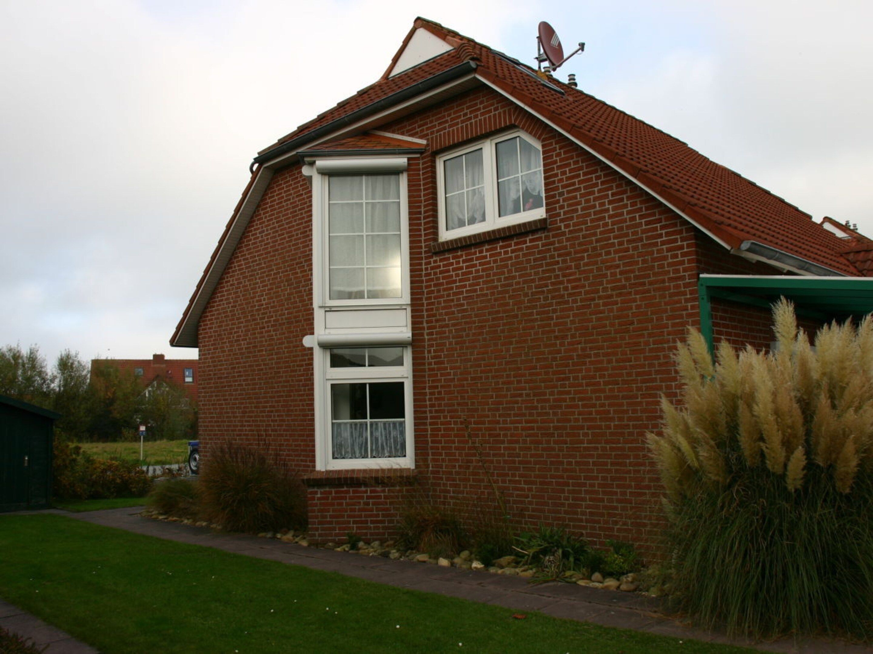 A single-story brick house with a pitched roof, a satellite dish, and a large window.