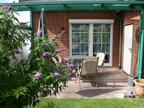 Eine Terrasse mit Tisch und Stühlen, eine Ziegelwand und ein grünes Sonnensegel.