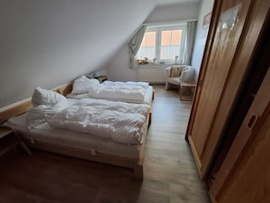 Ein Schlafzimmer mit zwei Betten, einem Holzschrank, einem Fenster mit Vorhängen und einem kleinen Tisch mit Dekoration.
