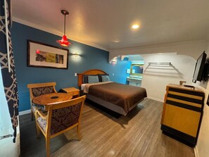 Een kamer met een bed, een bureau, een stoel, een hanglamp en een lijst aan de muur.