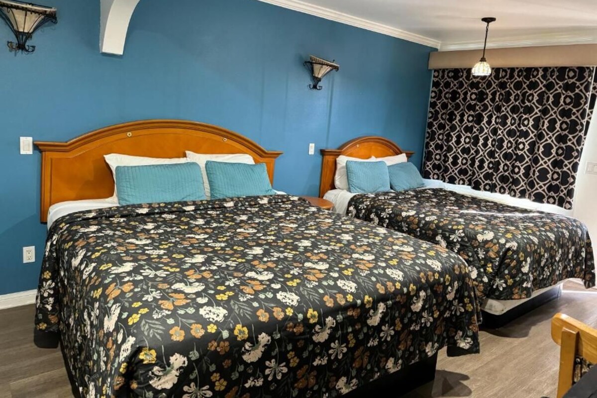 Een hotelkamer met twee bedden, een bed met een decoratieve spreidek, een blauwe accentmuur en een gordijn met dessin.