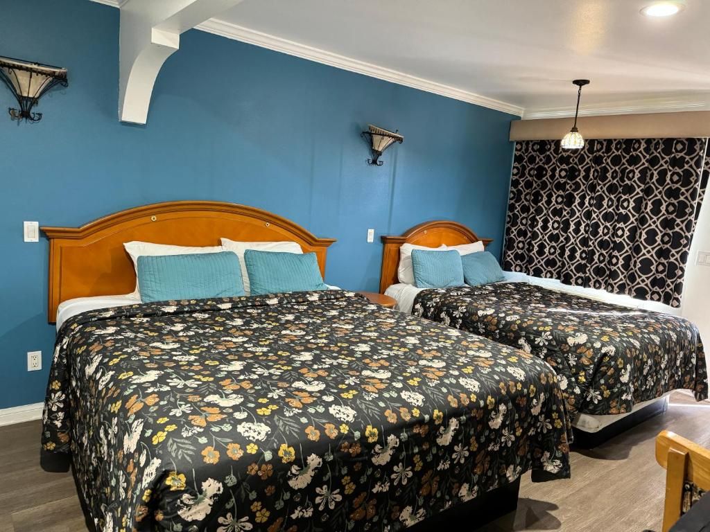 Ein Hotelzimmer mit zwei Betten, einer gemusterten Tagesdecke, einer blauen Akzentwand und einem gemusterten Vorhang.