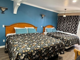 Quarto de hotel com duas camas, colcha estampada, parede azul e cortina padronada.