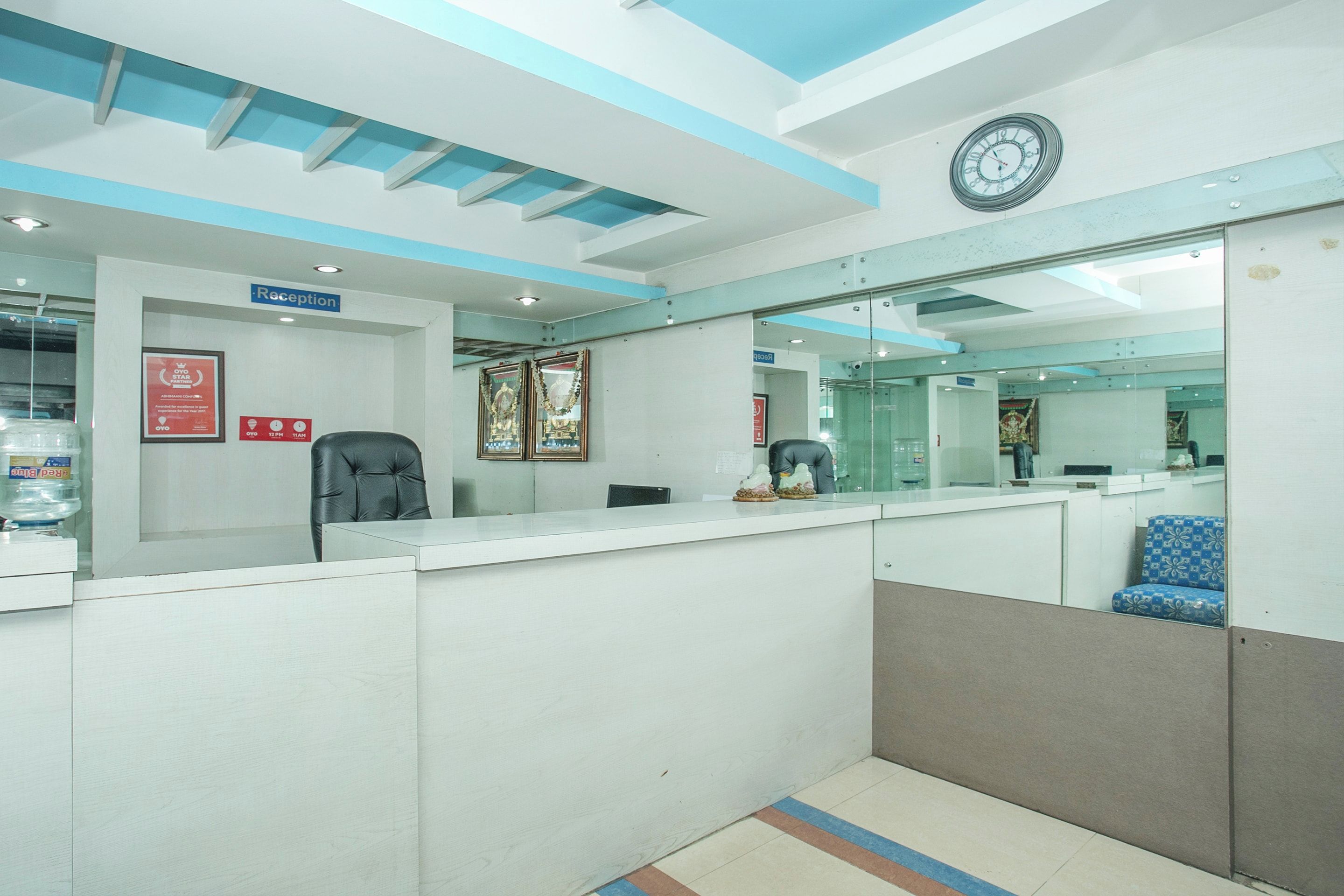 Zona de recepción con mostrador, un reloj, cuadros enmarcados y dispensador de agua.