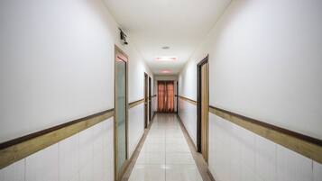 Un pasillo largo y estrecho con paredes blancas y suelo de baldosas, que conduce a una puerta al final.