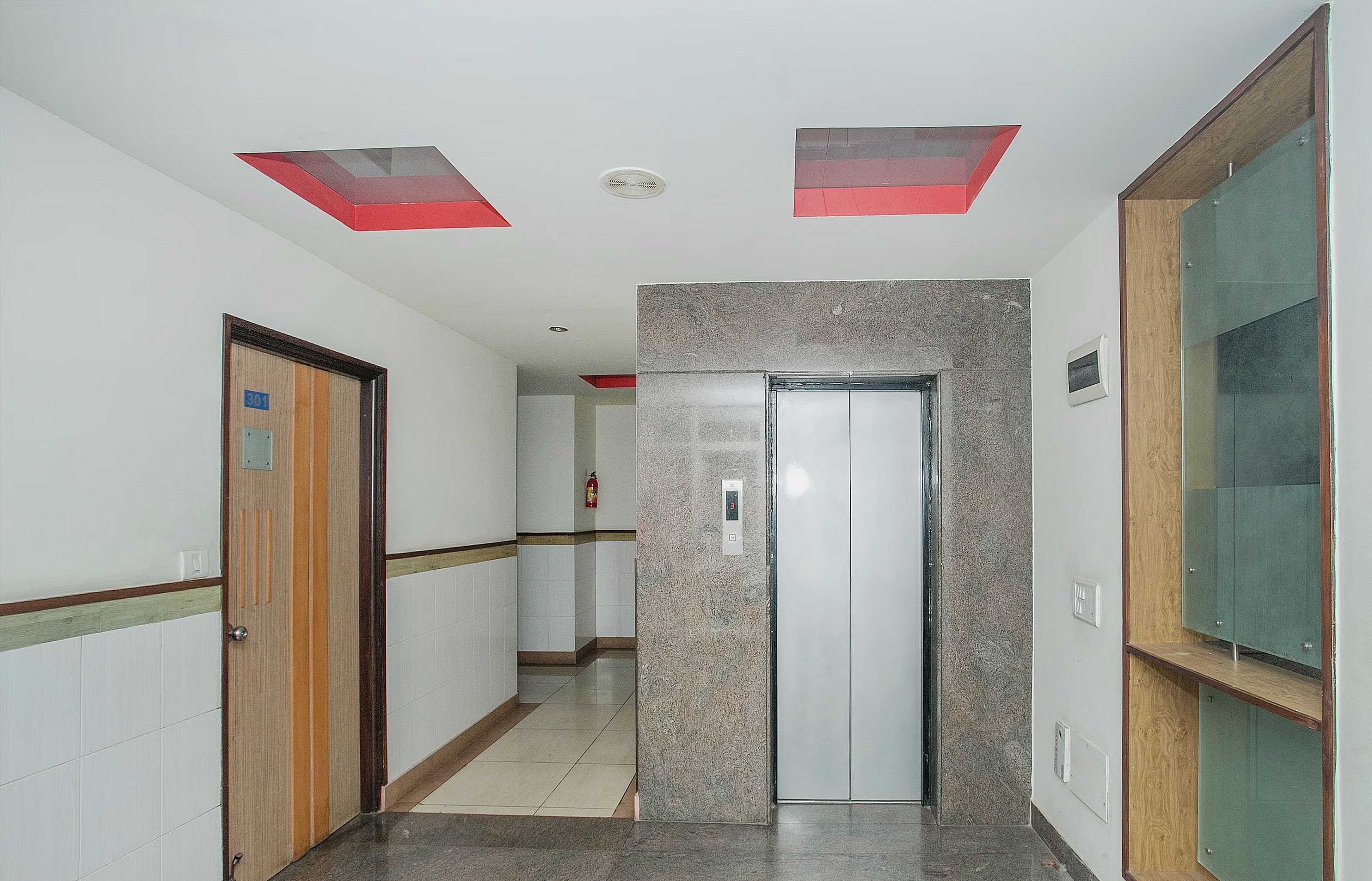 A hallway with a door, a fire extinguisher, and a wall-mounted elevator control panel.