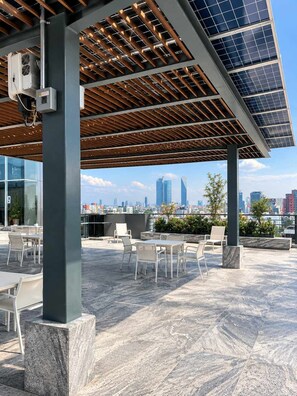 An outdoor seating area with tables and chairs, a pergola with solar panels, and a city skyline in the background. - Condesa Residence - Roma Luxury Suite 405 (Ciudad de México)