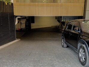 A parking area with a black SUV, a closed garage door, and a building with a sloped roof. - Condesa Residence - Roma Luxury Suite 407 (Ciudad de México)