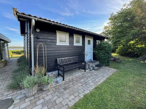 A wooden building with a bench and potted plants in front. - Summer house with views over Lammefjorden (Grevinge)