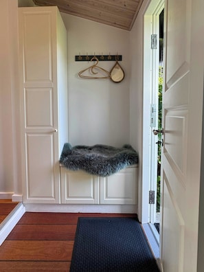 A hallway with a wooden floor, a black doormat, a fur rug, a coat rack, and a white door. - Summer house with views over Lammefjorden (Grevinge)
