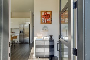 A modern kitchen with a stainless steel refrigerator, a dining area with a wicker chair, and a framed poster on the wall. - 4 Modern Townhomes | Balconies | Walk to Cafés + Shops | Lischey Full Buyout (Nashville)