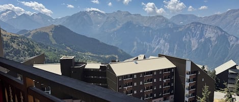A mountain view from a balcony with a wooden railing, overlooking a residential area with multi-story buildings and a clear sky.