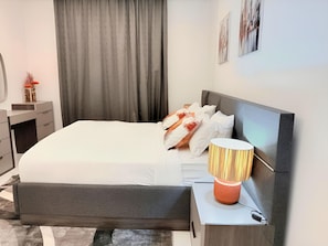 A modern bedroom with a bed, bedside table, lamp, and artwork on the wall. - Rooftop Pool with Riverview 3 bedroom apartment (Kinshasa)