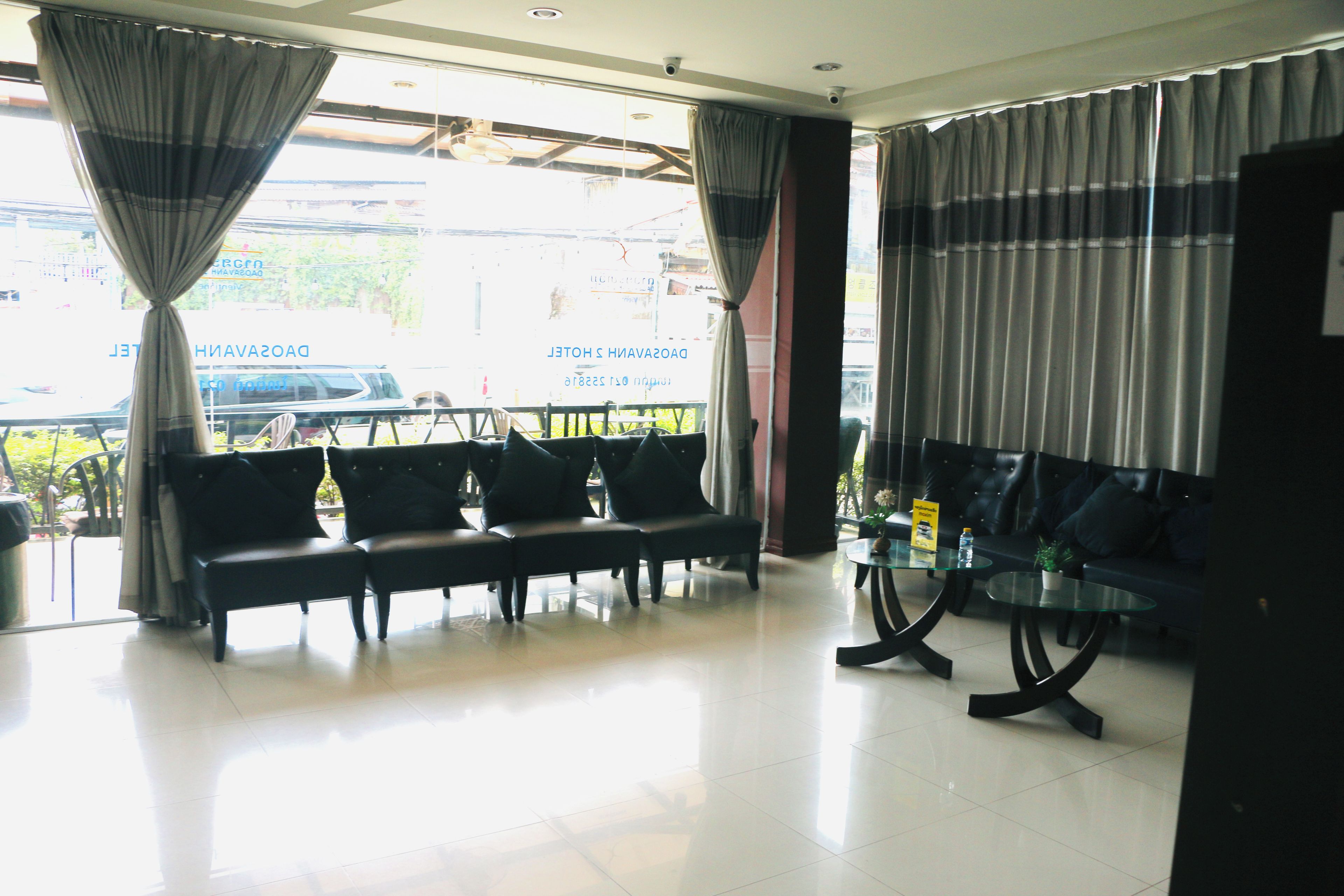 A hotel lobby with a seating area, a reception desk, and a view of the street outside.