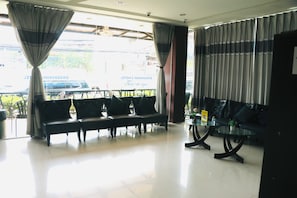 Un vestíbulo de hotel con zona de estar, mostrador de recepción y vista a la calle.
