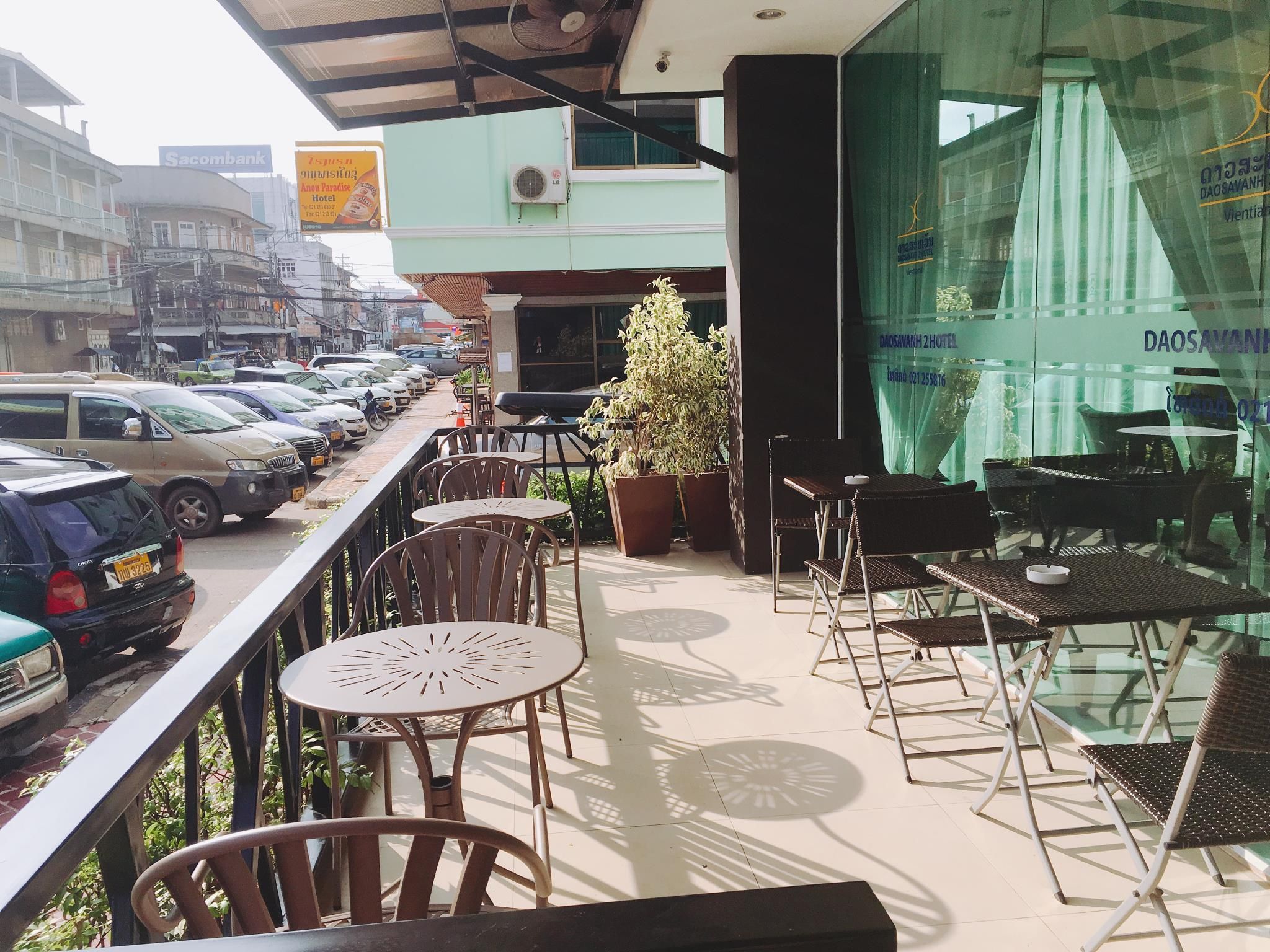A balcony with outdoor seating, a view of parked cars, and a building with signage.