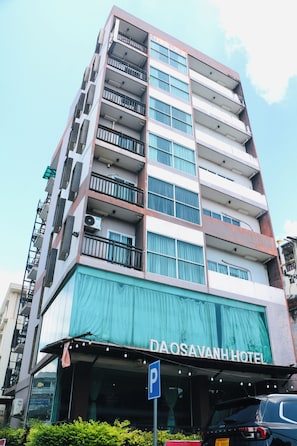 Un hotel de varios pisos con balcones en cada planta, un cartel visible que dice 'DAOSAVANH HOTEL' y un letrero de estacionamiento que indica una zona de aparcamiento.