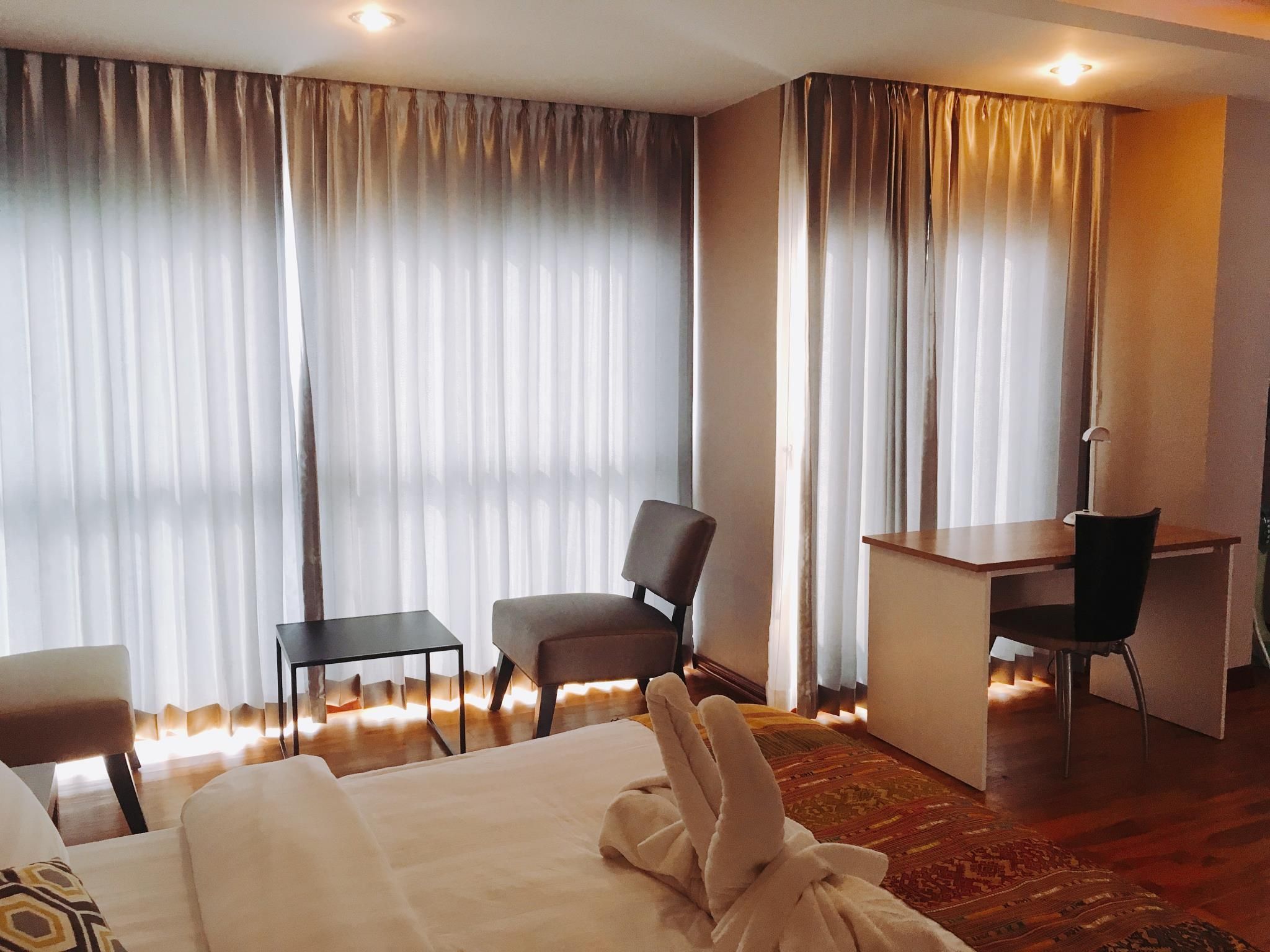 A hotel room with a bed, two chairs, a desk, and a large window with curtains.