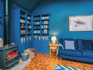 Ein Zimmer mit blauer Wand, einem Bücherregal, einer Couch, einem Kamin und einem gerahmten Bild.