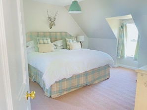 Une chambre à coucher avec un lit, une tête de lit, une lampe et une fenêtre avec des rideaux.