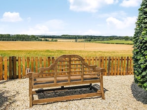 A wooden bench in a gravel area with a view of a field and distant hills. - There’s lots to love here. (Kelso)