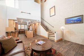 A spacious living area with a sofa, coffee table, and a view of the kitchen and stairs. - Park Ave 235 | Heated Pool | Hot Tub | Remodeled | Stone Fireplace | Granite Kitchen | Laundry (Park City)