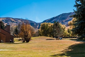 A grassy area with a building on the left and a mountain in the background. - Park Ave 236 | Heated Pool | Hot Tub | Mtn Views | Trail-Side by Golf Course | Laundry | Near PCMR (Park City)