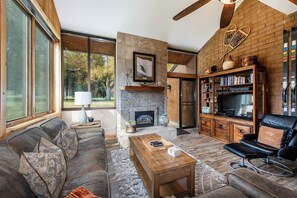 A modern living room with a fireplace, a leather sofa, a coffee table, and a bookshelf. - Park Ave 236 | Heated Pool | Hot Tub | Mtn Views | Trail-Side by Golf Course | Laundry | Near PCMR (Park City)