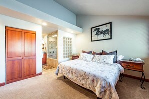 A bedroom with a bed, a wooden wardrobe, a bathroom with a glass door, and a framed artwork on the wall. - Park Ave 245 | Heated Pool | Hot Tub | A/C | Laundry | Trail-Side by Golf Course | Near PCMR (Park City)