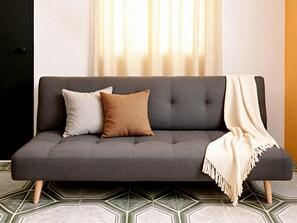 Ein graues Sofa mit zwei Kissen und einer Decke auf einem gemusterten Boden.